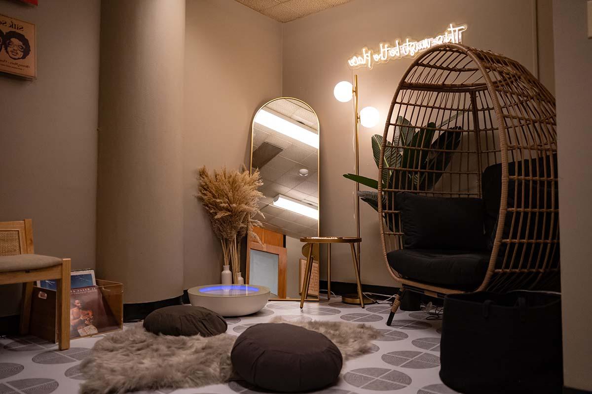 Image of a room with low lighting, a hanging chair with footrest, and cushions and a fluffy carpet on the floor.